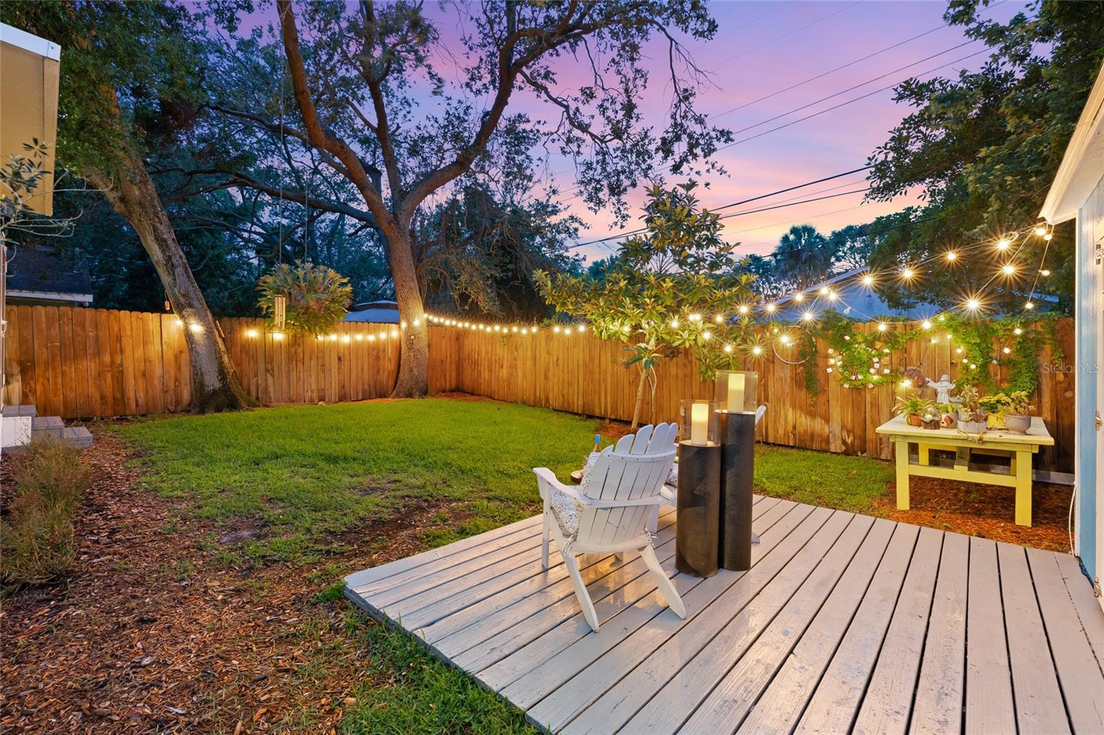 Mature trees and string lighting set the mood in this inviting backyard space, ideal for gatherings or unwinding after sunset.