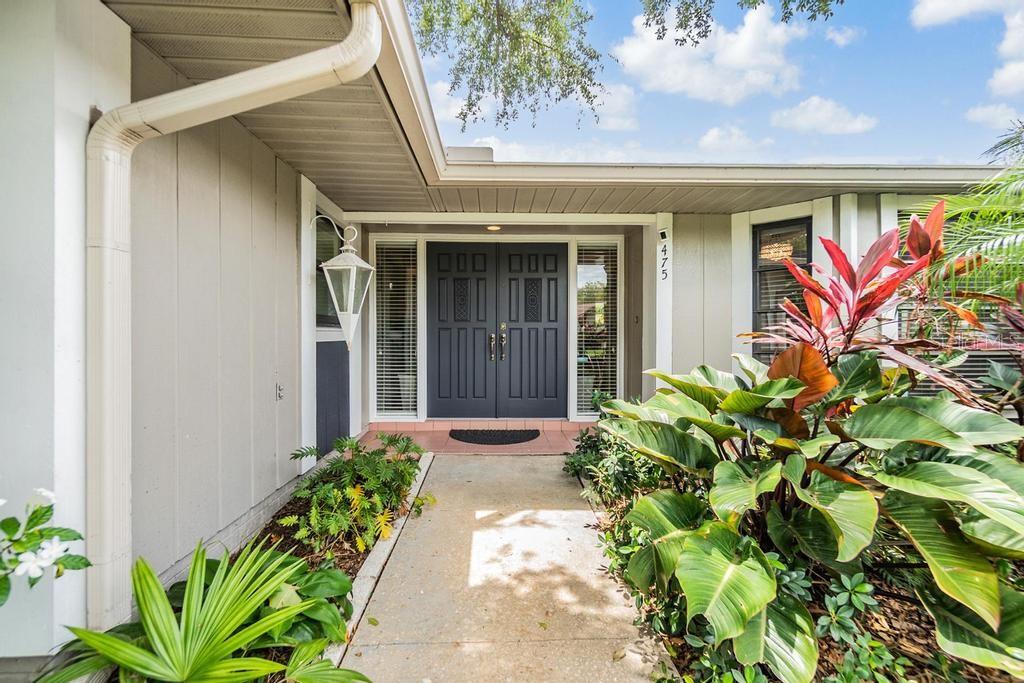 Front entry way with lush, mature landscaping and elegant double front doors framed with glass sidelights