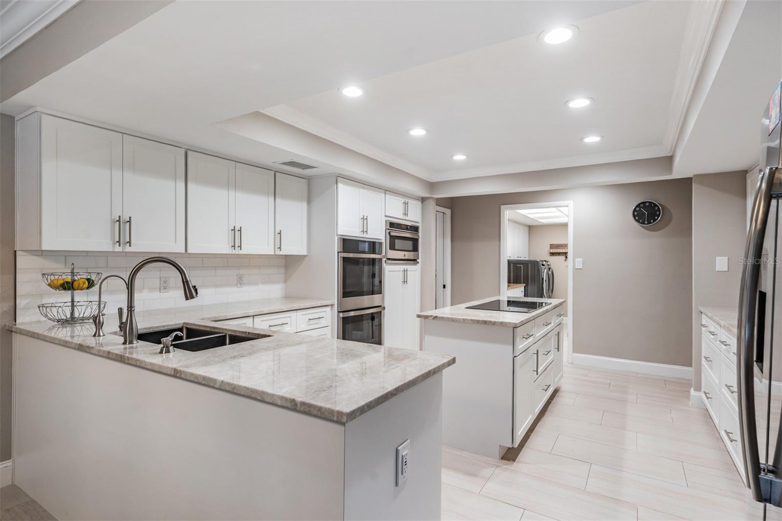 Chef's dream kitchen - blends style and functionality. Well-equipped with stainless steel appliances—including 2 GE Profile Smart built-in ovens, a convection microwave, a sleek induction cooktop on the oversized island, beautiful Quartzite countertops, marble tile backsplash, and recessed lighting. Abundant cabinetry, a custom-shelved pantry, and generous counter space make organization and meal prep effortless.