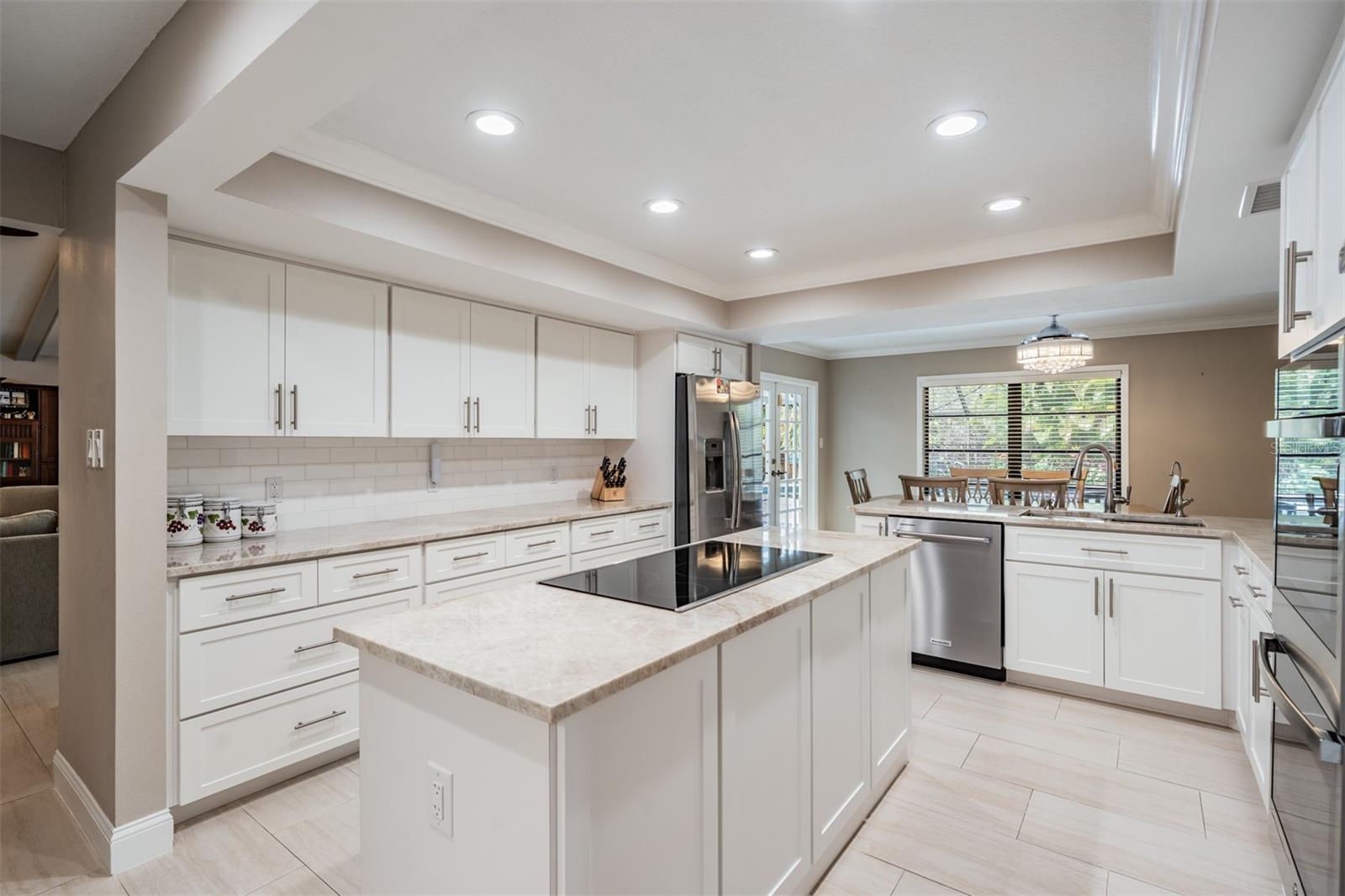 The stunning, eat-in kitchen blends style and functionality. Well-equipped with stainless steel appliances—including 2 GE Profile Smart built-in ovens, a convection microwave, a sleek induction cooktop on the oversized island, beautiful Quartzite countertops, marble tile backsplash, and recessed lighting. Abundant cabinetry, a custom-shelved pantry, and generous counter space make organization and meal prep effortless.