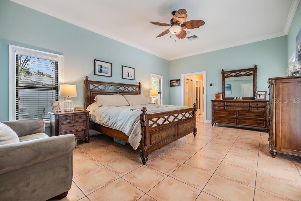 The primary suite is a luxurious retreat, featuring private pool access through sliding glass doors, terra-cotta tile, designer fan and a boutique-style 14’x8’ walk-in closet with custom shelving, complemented by two additional wall closets.