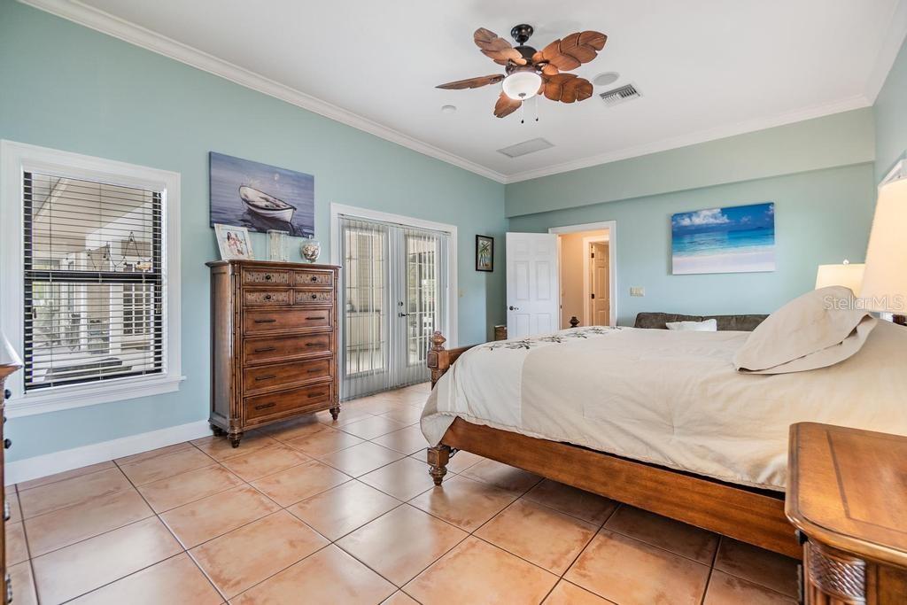 The primary suite is a luxurious retreat, featuring private pool access through sliding glass doors, terra-cotta tile, designer fan and a boutique-style 14’x8’ walk-in closet with custom shelving, complemented by two additional wall closets.