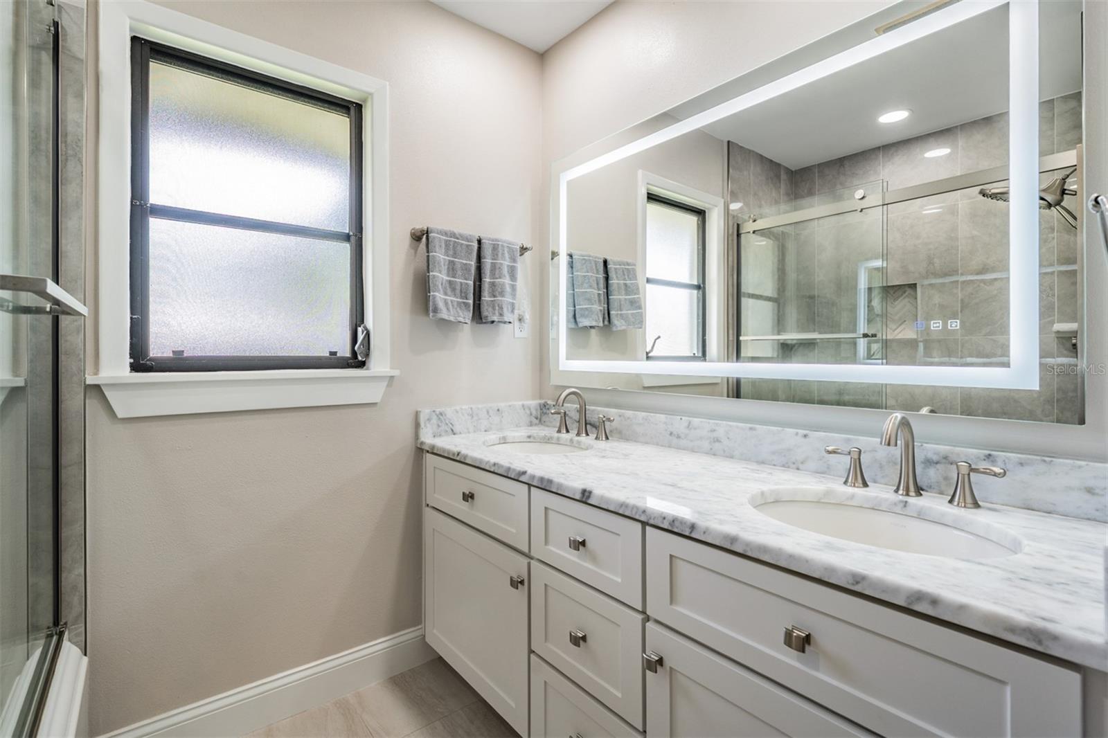 Beautifully updated bathroom featuring a marble-topped dual-sink vanity and a tub/shower combination