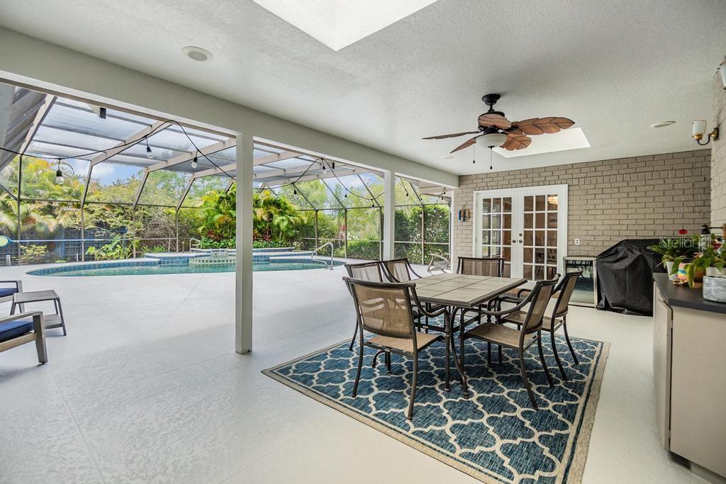 Step outside to the expansive pool deck, where a covered seating area with skylights and a ceiling fan creates the perfect spot to unwind. Surrounded by lush tropical landscaping, the sparkling Gulfstream saltwater pool features a gleaming pebble sheen finish, self-cleaning system, and a tranquil spillover spa with fountain.