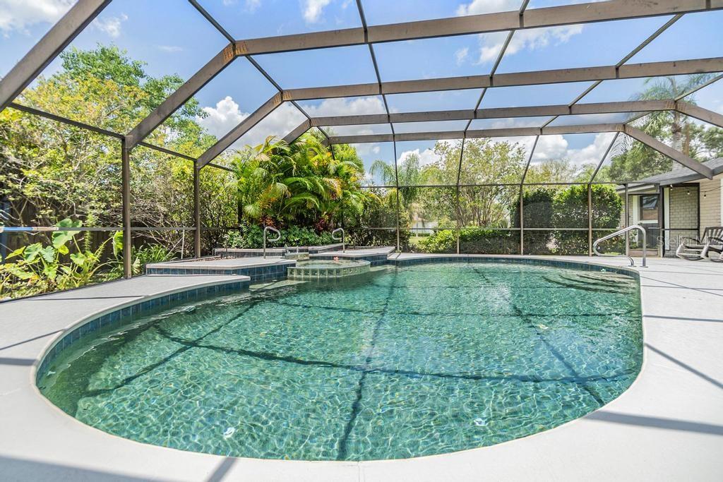Step outside to the expansive pool deck, where a covered seating area with skylights and a ceiling fan creates the perfect spot to unwind. Surrounded by lush tropical landscaping, the sparkling Gulfstream saltwater pool features a gleaming pebble sheen finish, self-cleaning system, and a tranquil spillover spa with fountain.