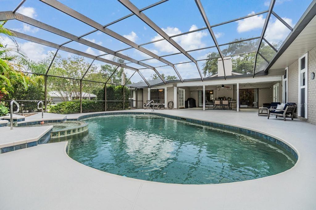 Step outside to the expansive pool deck, where a covered seating area with skylights and a ceiling fan creates the perfect spot to unwind. Surrounded by lush tropical landscaping, the sparkling Gulfstream saltwater pool features a gleaming pebble sheen finish, self-cleaning system, and a tranquil spillover spa with fountain.