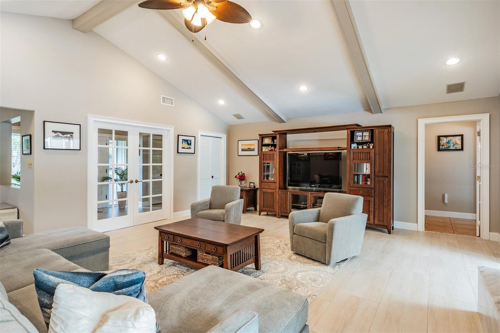 At the heart of the home, the expansive living room offers a warm and sophisticated ambiance, accented by neutral tones, gorgeous tile flooring, and a vaulted ceiling with exposed wood beams.
