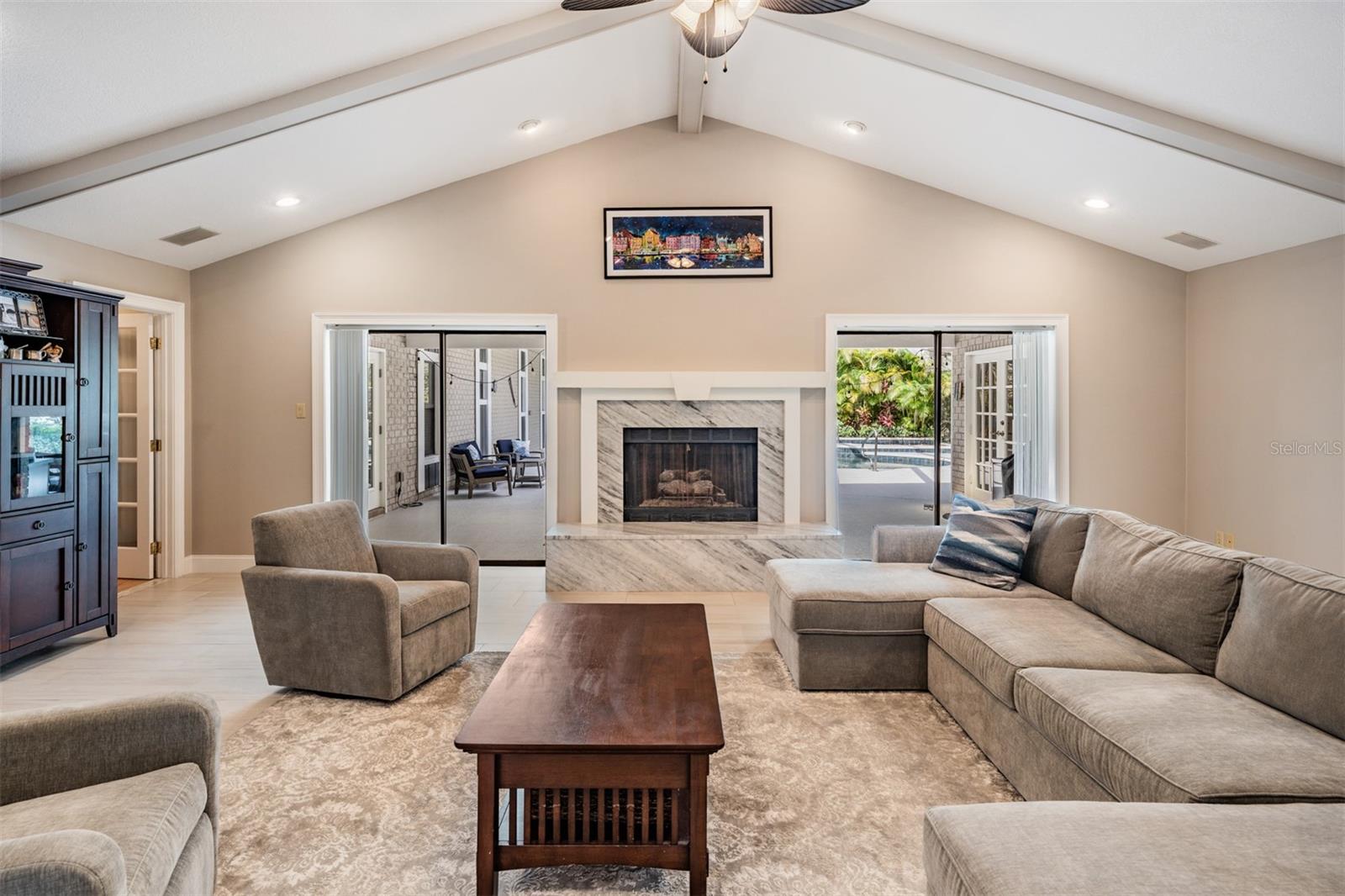 . A gas fireplace with marble accents and polished hearth serves as a striking focal point, flanked by two sliding glass doors that open to the pool area. This beautifully designed space is perfectly suited for both relaxed family time and upscale entertaining.