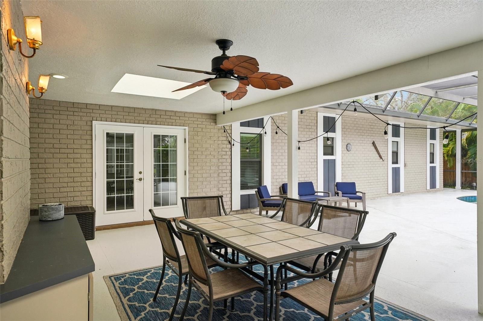 Step outside to the expansive pool deck, where a covered seating area with skylights and a ceiling fan creates the perfect spot to unwind. Surrounded by lush tropical landscaping, the sparkling Gulfstream saltwater pool features a gleaming pebble sheen finish, self-cleaning system, and a tranquil spillover spa with fountain.