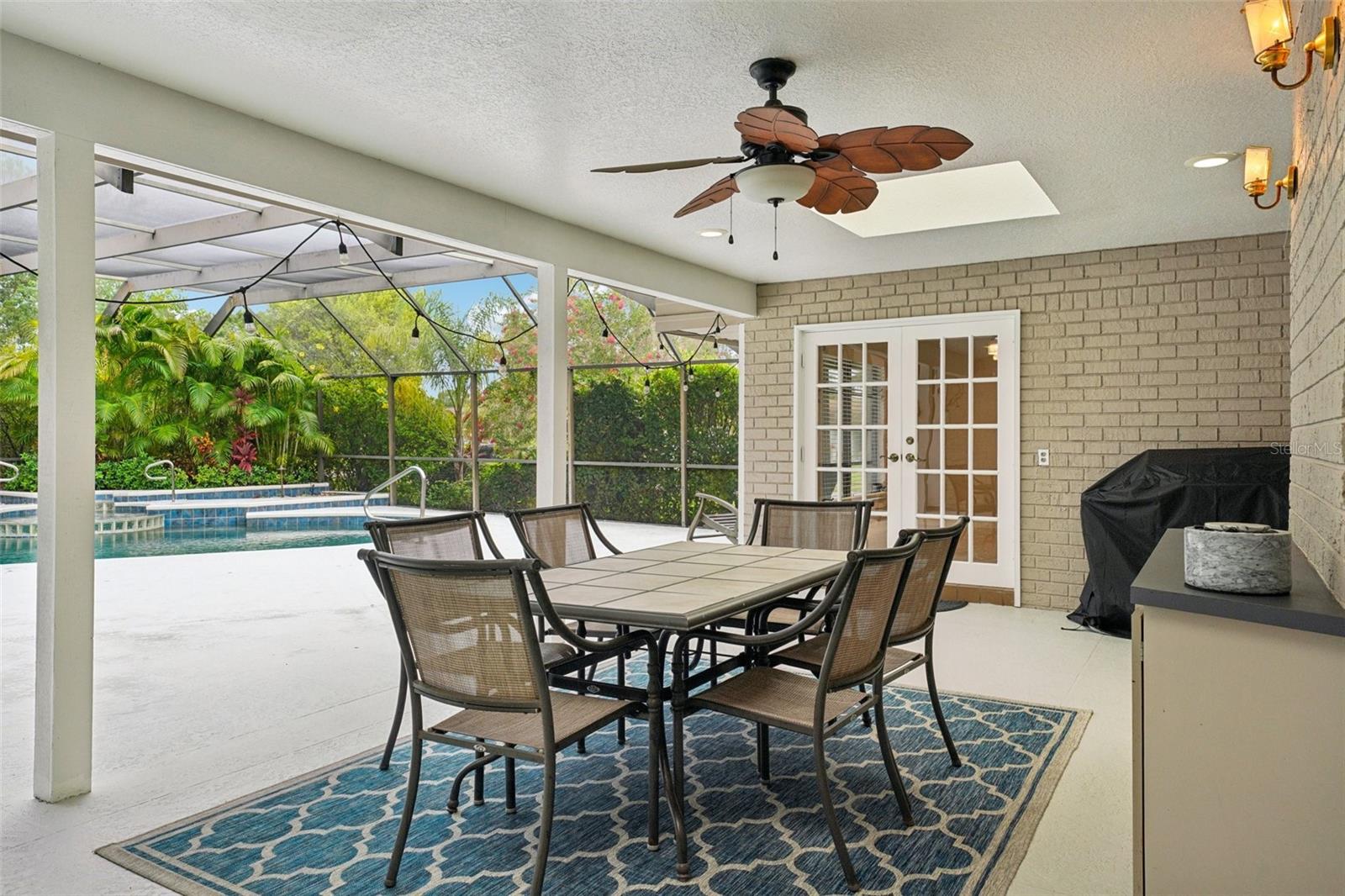 Step outside to the expansive pool deck, where a covered seating area with skylights and a ceiling fan creates the perfect spot to unwind. Surrounded by lush tropical landscaping, the sparkling Gulfstream saltwater pool features a gleaming pebble sheen finish, self-cleaning system, and a tranquil spillover spa with fountain.