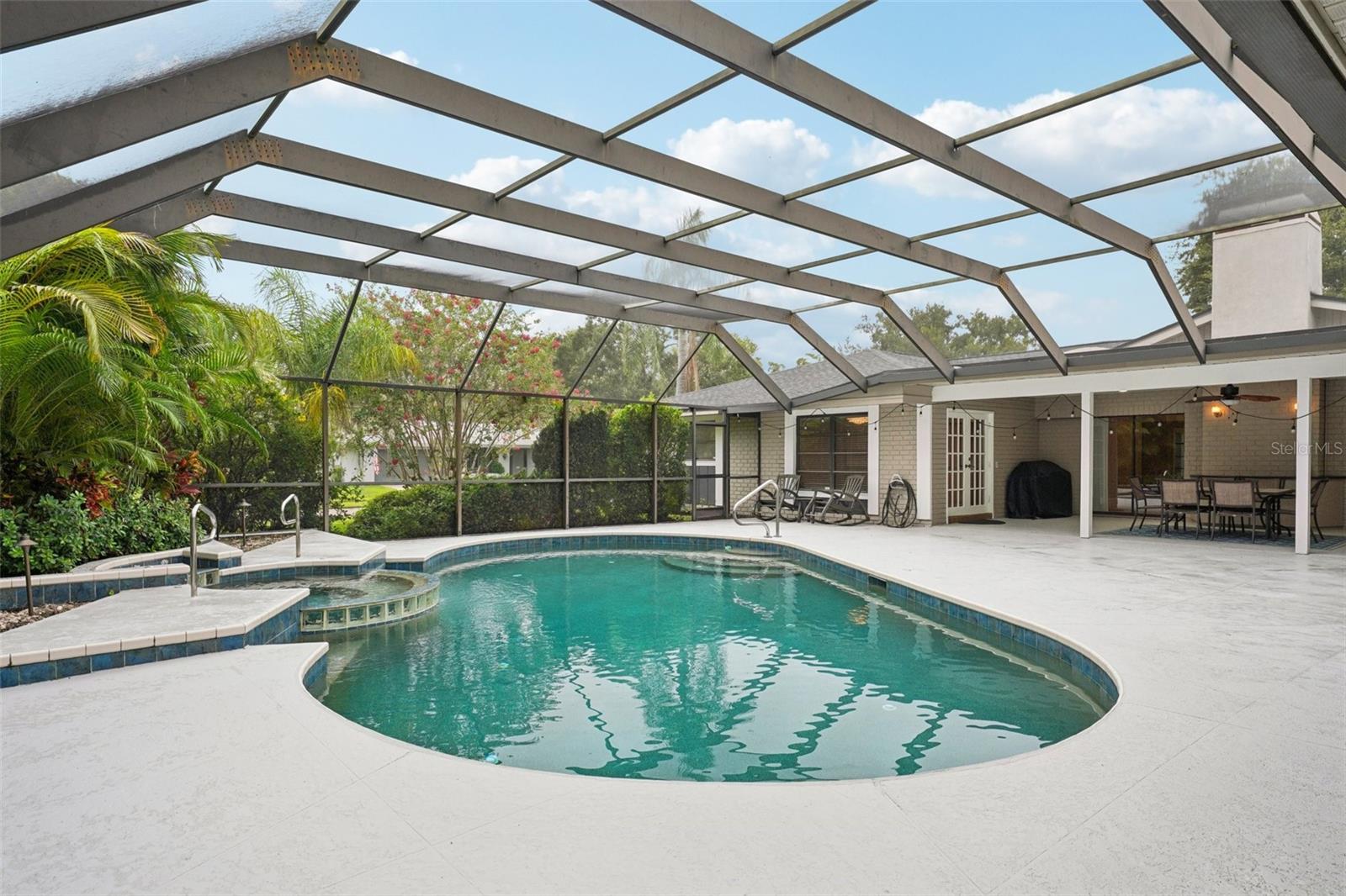 Step outside to the expansive pool deck, where a covered seating area with skylights and a ceiling fan creates the perfect spot to unwind. Surrounded by lush tropical landscaping, the sparkling Gulfstream saltwater pool features a gleaming pebble sheen finish, self-cleaning system, and a tranquil spillover spa with fountain.