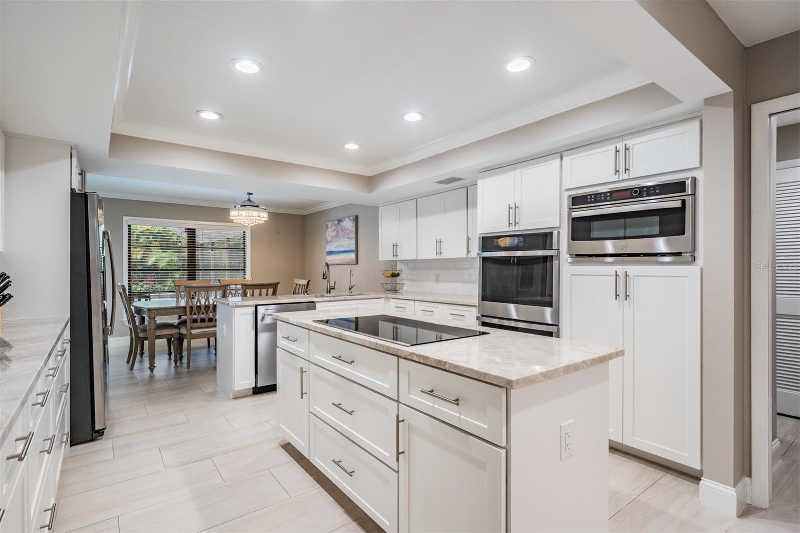 Chef's dream kitchen - blends style and functionality. Well-equipped with stainless steel appliances—including 2 GE Profile Smart built-in ovens, a convection microwave, a sleek induction cooktop on the oversized island, beautiful Quartzite countertops, marble tile backsplash, and recessed lighting. Abundant cabinetry, a custom-shelved pantry, and generous counter space make organization and meal prep effortless.