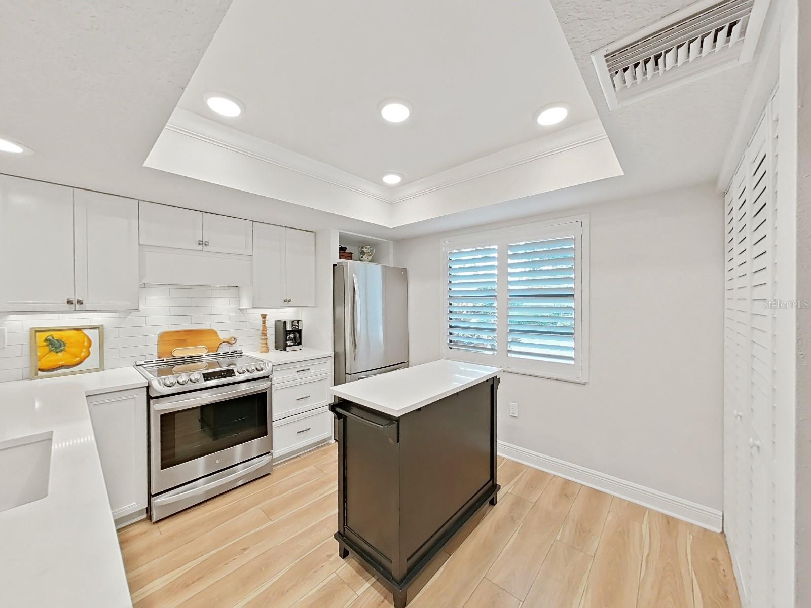 Custom vent hood (vented to the outside) above the slide-in range. A central island with quartz top provides additional space for food prep.
