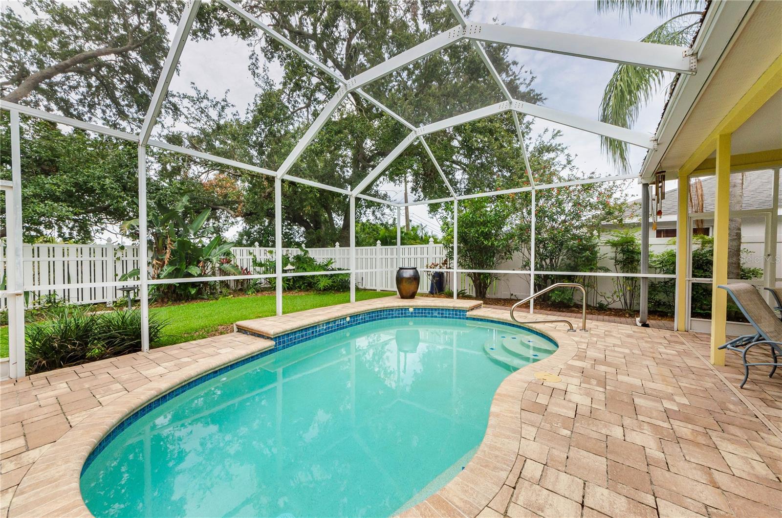 Gorgeous heated swimming pool with Pebble Tech interior surrounded by brick pavers, screen cage overhead, fenced yard.