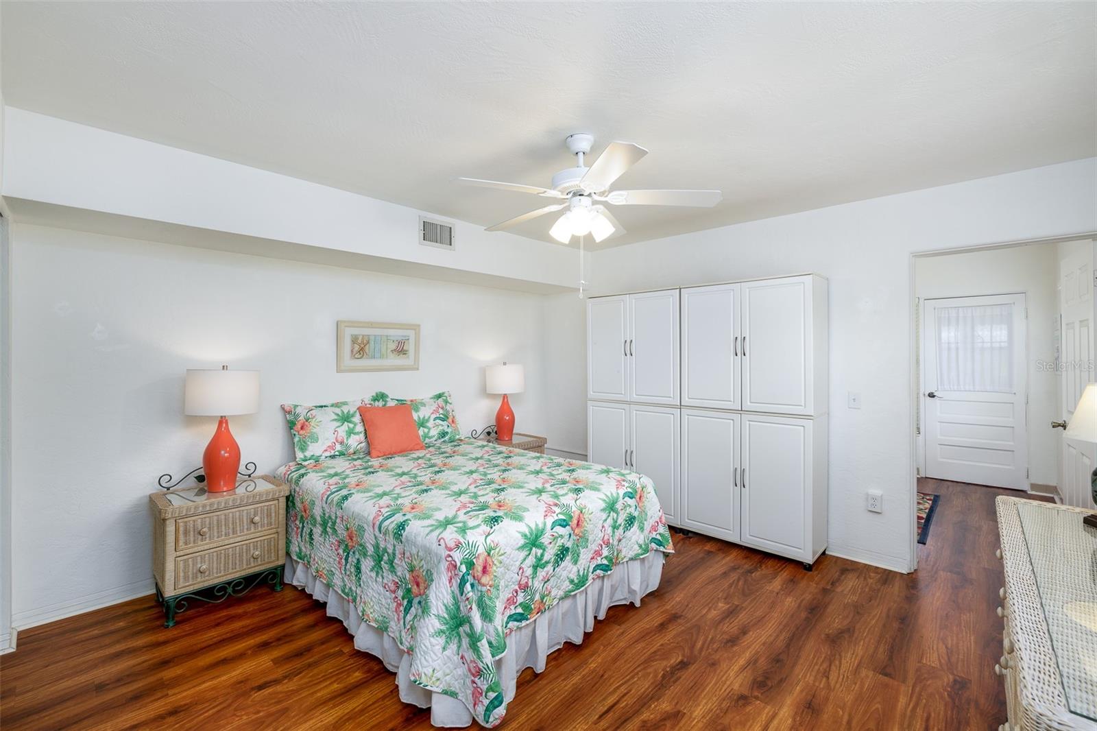 The generously sized bedroom offers plenty of room to unwind, with a ceiling fan, wood-look flooring, and charming tropical decor. Built-in cabinetry provides excellent storage.