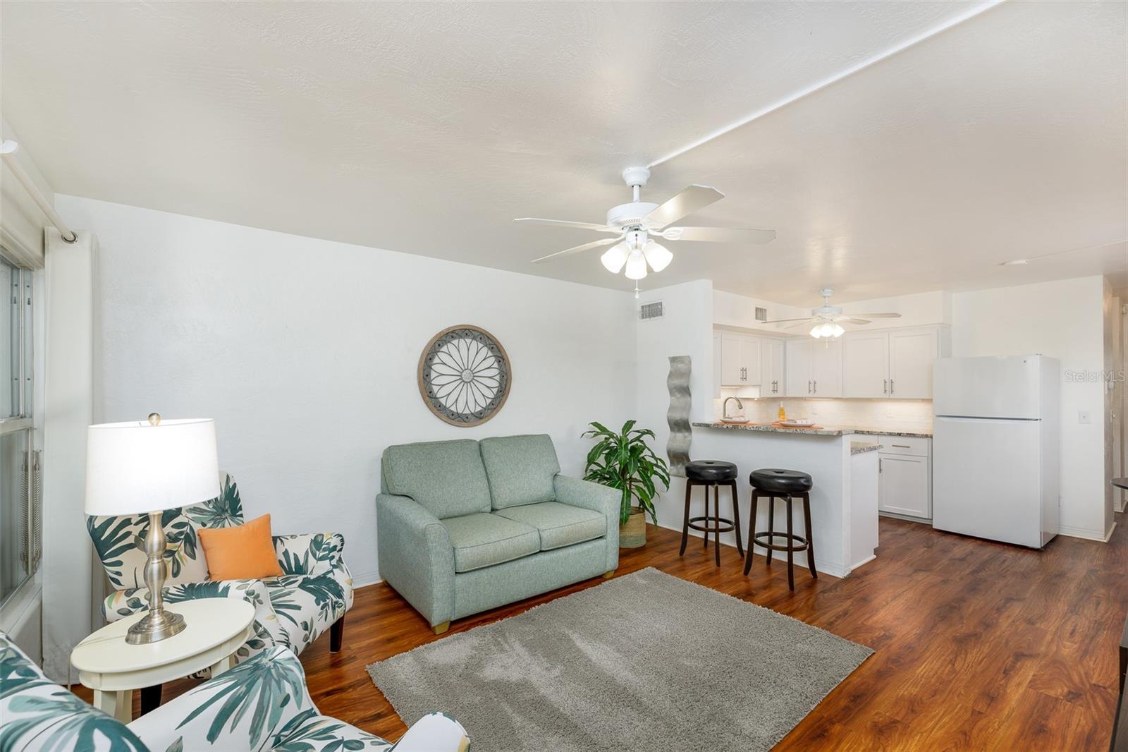 The spacious living room flows effortlessly into the renovated kitchen, with wood-look flooring, updated lighting, and coastal-inspired furnishings that stay!