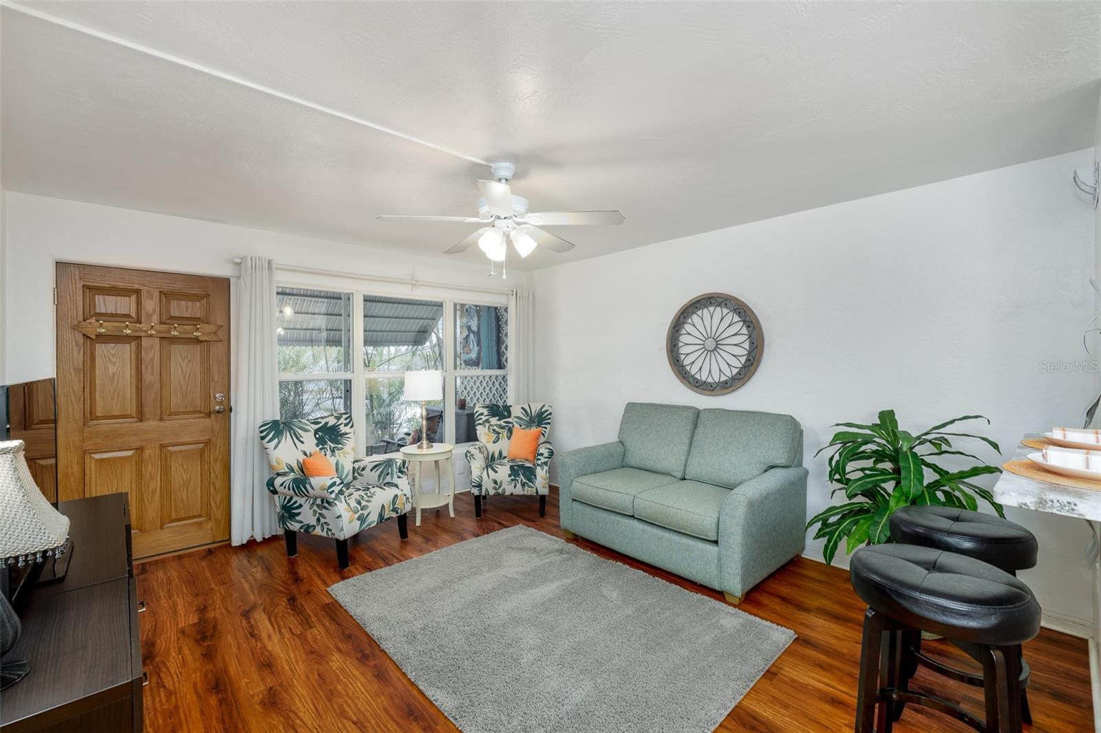 This cozy living space features front-facing hurricane-impact windows, updated window treatments, and ceiling fans throughout for comfort and energy efficiency.