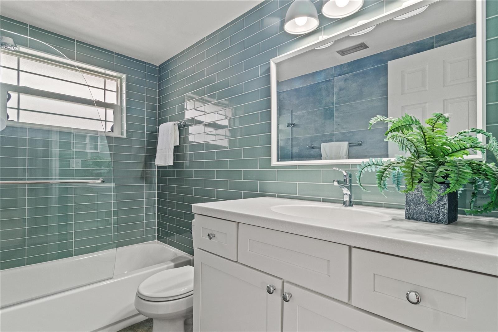 The guest bath has a beachy vibe with glass tiles in coastal colors reminiscent  of sea glass