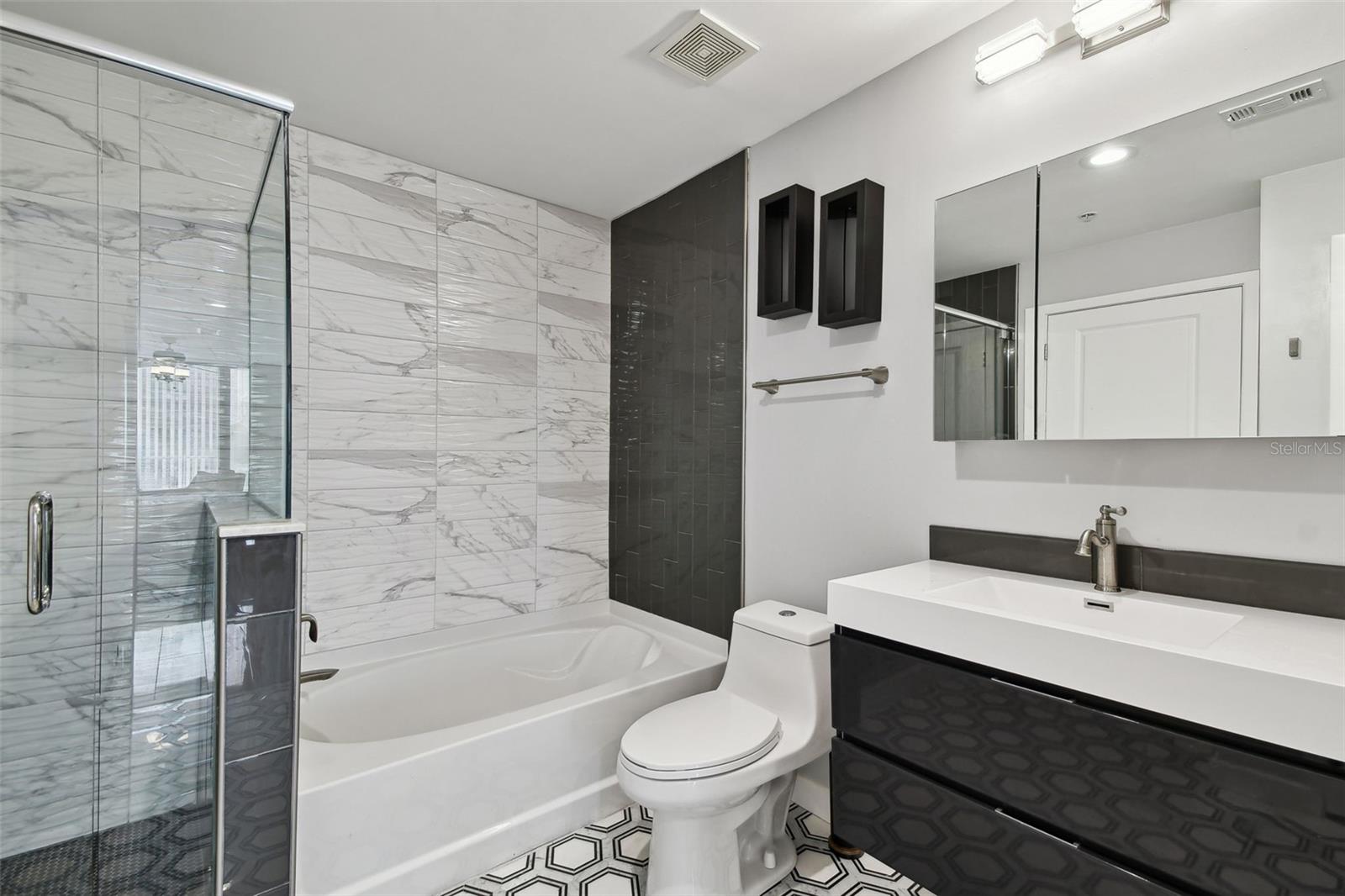 This thoughtfully updated guest bathroom boasts bold geometric tile flooring, a floating vanity, modern lighting, and a sleek black-tiled shower wall.