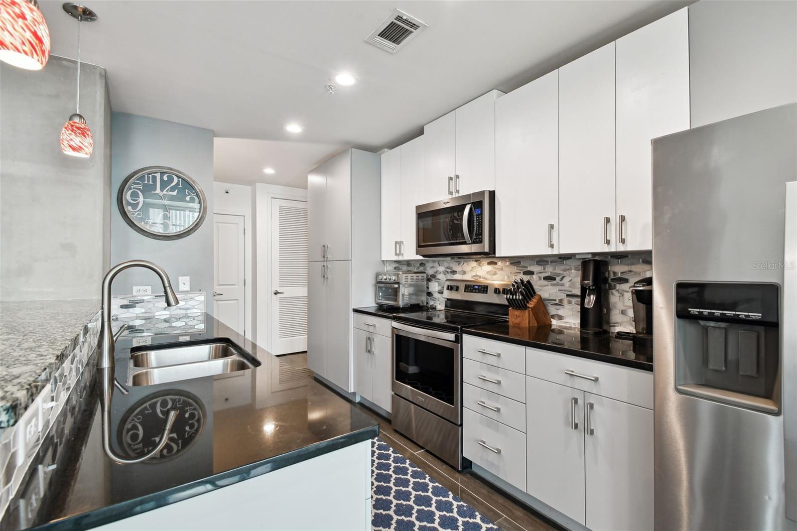 The sleek, open kitchen features granite countertops, stainless steel appliances, high-gloss cabinetry, and a stylish glass tile backsplash.