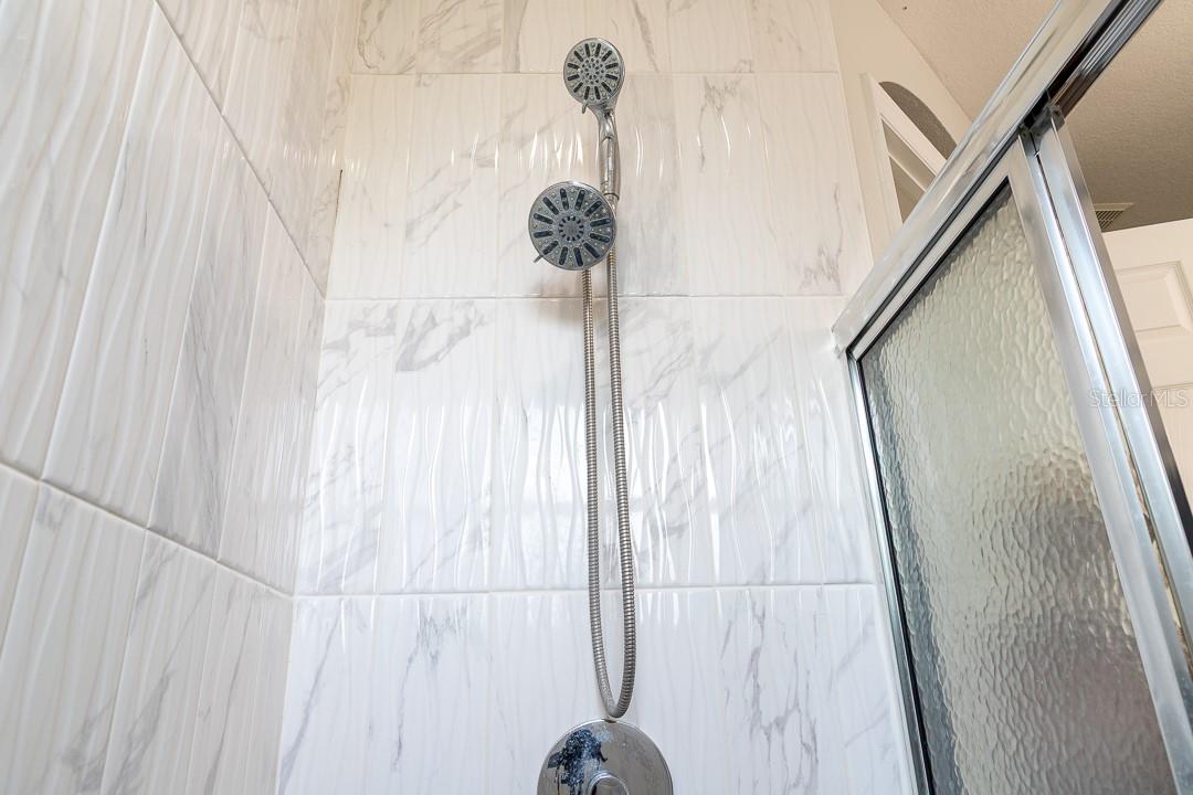 Dual shower head in en suite bathroom with a obscure two way sliding glass door.