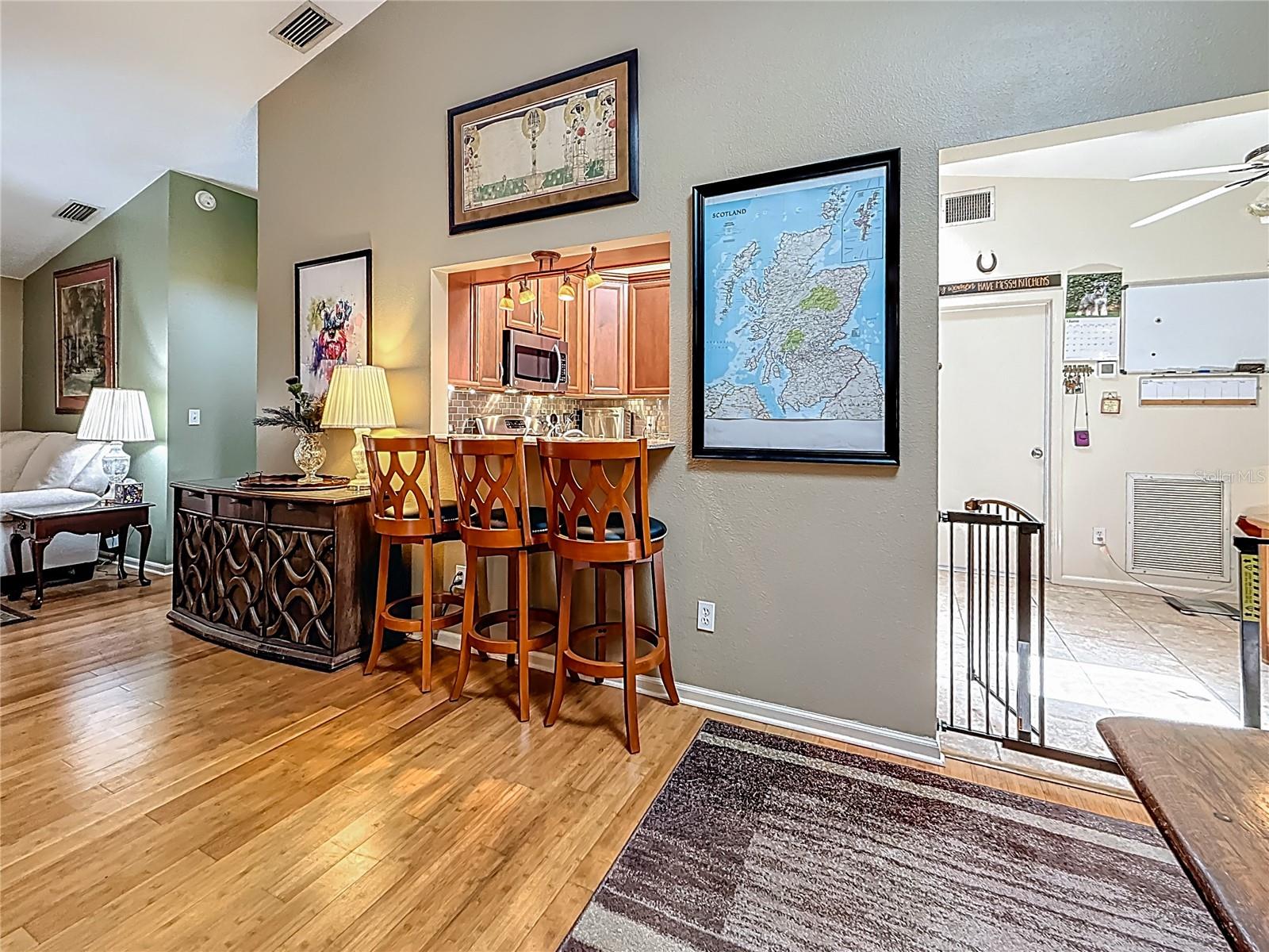 You are in the dining room looking towards the breakfast bar. Next to the sideboard on your left is the entryway to the Primary Bedroom Suite. Entrance to the updated kitchen is through the opening towards your right.