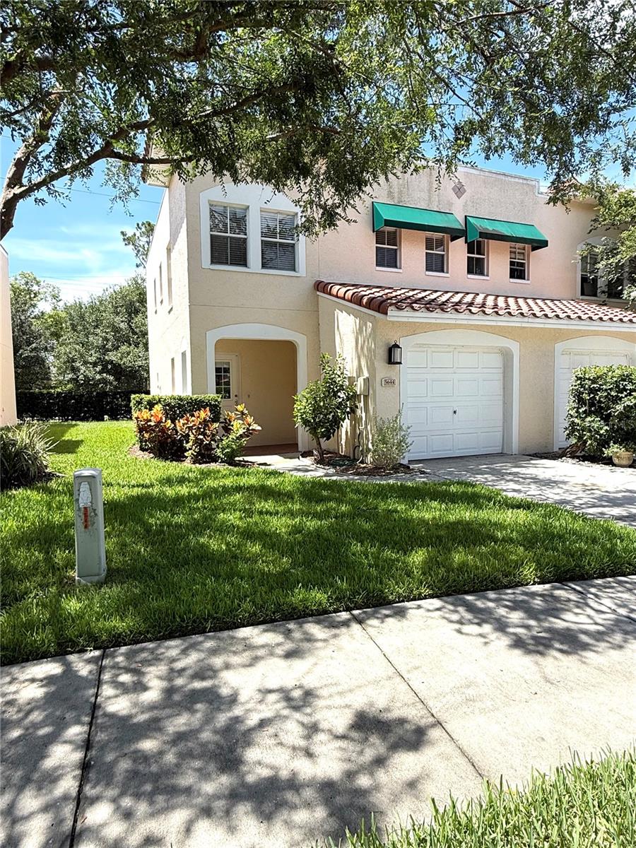 Charming and full of curb appeal, this tan townhouse stands out with classic green awnings, a crisp white garage, and colorful plants that bring the entryway to life. A warm, welcoming vibe from the moment you arrive!