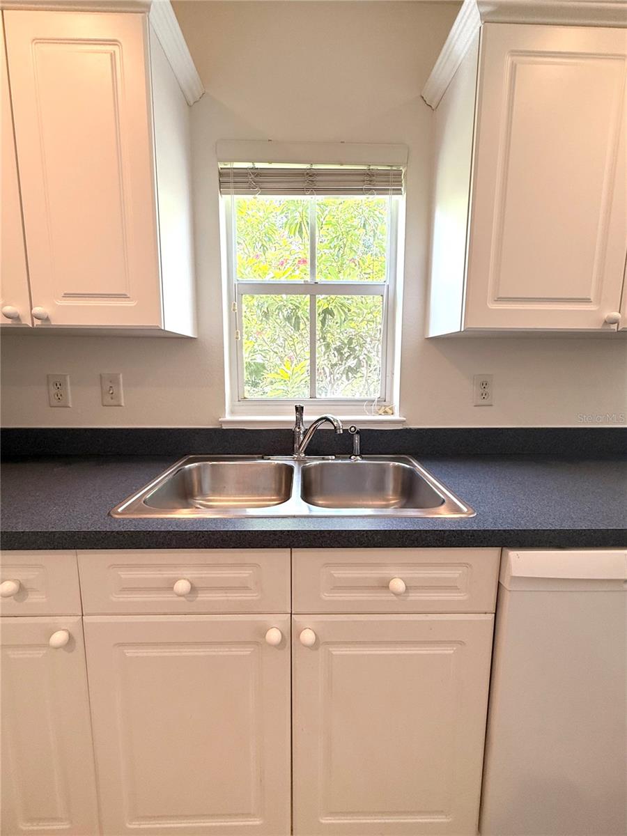 Washing dishes feels like a delight at this kitchen sink, where a window above frames a vibrant view of blooming red flowers. Bathed in natural light, it’s a picturesque spot that brings a touch of nature and warmth into your everyday routine.