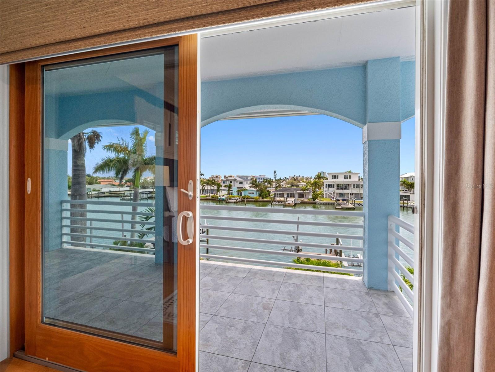 French impact doors open to wide, covered balcony from the primary suite.