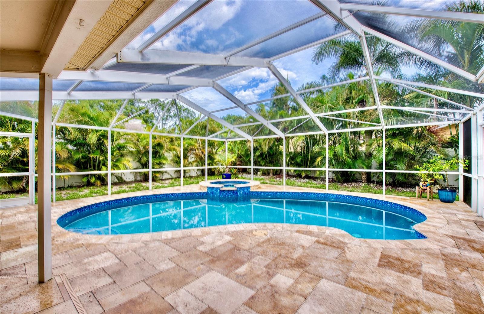 250 sq ft POOL PATIO OASIS is framed by elegant travertine pavers, with lush palm trees just beyond the pool cage offering natural privacy and a true tropical feel.