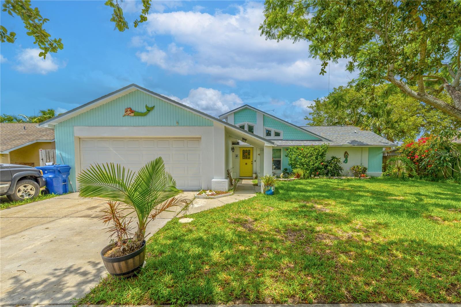 Charming 3-bedroom, 2-bath home in Holiday Lakes West. With its cheerful coastal vibe and welcoming front entry, this home exudes personality and curb appeal. A covered walkway leads to a bright front door that adds a pop of character. The architectural lines and vaulted roof peaks give the home a distinctive look, while mature shade trees and lush tropical landscaping offer both beauty and privacy. A two-car garage provides convenience, and there's plenty of space for additional parking.