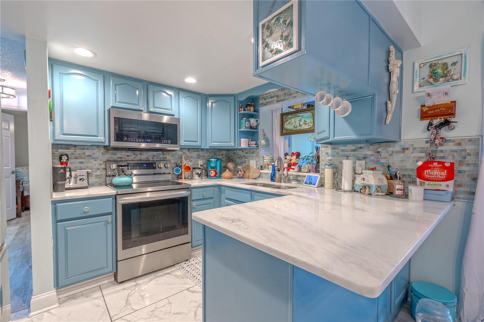Recessed lighting adds brightness, and a sleek mosaic tile backsplash gives the kitchen a modern touch. Abundant cabinetry offers ample storage, with thoughtful open shelving for displaying favorite mugs or everyday essentials.