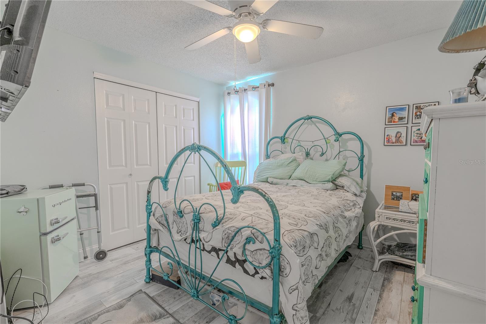 The third bedroom features a bright and cheerful atmosphere with wood-look vinyl flooring, a ceiling fan, and a double-door closet for storage. A large window allows for great natural light