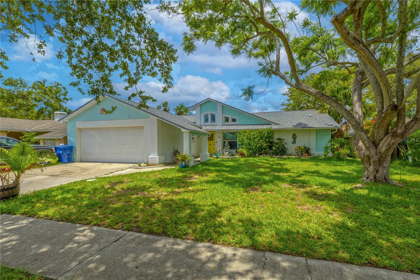 Charming 3-bedroom, 2-bath home in Holiday Lakes West. With its cheerful coastal vibe and welcoming front entry, this home exudes personality and curb appeal. A covered walkway leads to a bright front door that adds a pop of character. The architectural lines and vaulted roof peaks give the home a distinctive look, while mature shade trees and lush tropical landscaping offer both beauty and privacy. A two-car garage provides convenience, and there's plenty of space for additional parking.