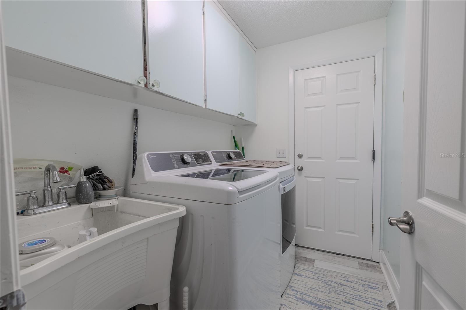 This dedicated laundry room offers both function and convenience with a full-size washer and dryer set, utility sink, and upper cabinets for extra storage. The room is well-lit and features easy-to-clean flooring, making laundry day a breeze. A door leads directly to the garage, adding easy access for household chores or coming in from outside. With everything you need in one place, this space helps keep the rest of the home neat and organized.