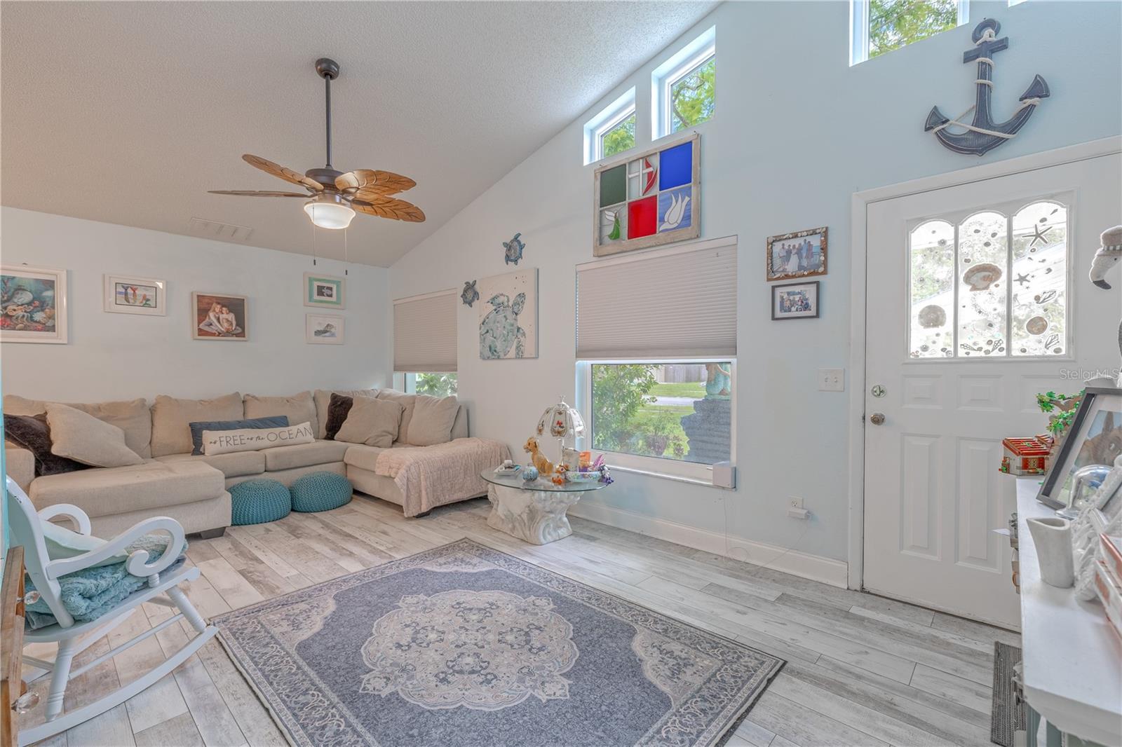 A bright and inviting living room where coastal charm meets everyday comfort. Vaulted ceilings with clerestory windows fill the space with natural light, creating an open, airy atmosphere