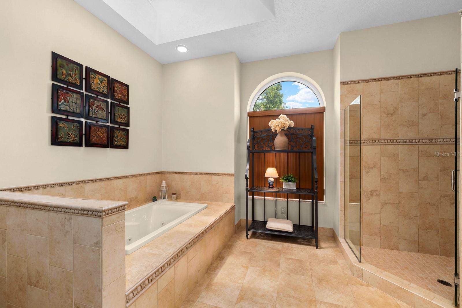 The updated primary ensuite features a walk-in shower, soaking tub, a large vanity with updated lighting, dual sinks, recessed lighting, and a beautiful window that could bring in lots of natural light.