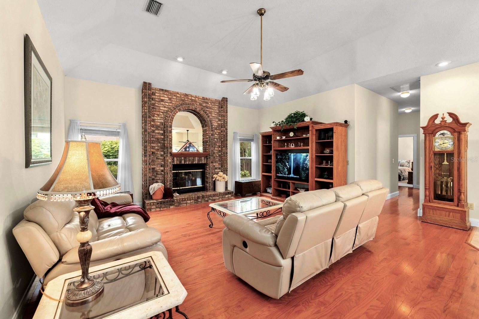 The Great Room features a wood-burning brick fireplace, volume ceilings, hardwood floors, and a lighted ceiling fan!