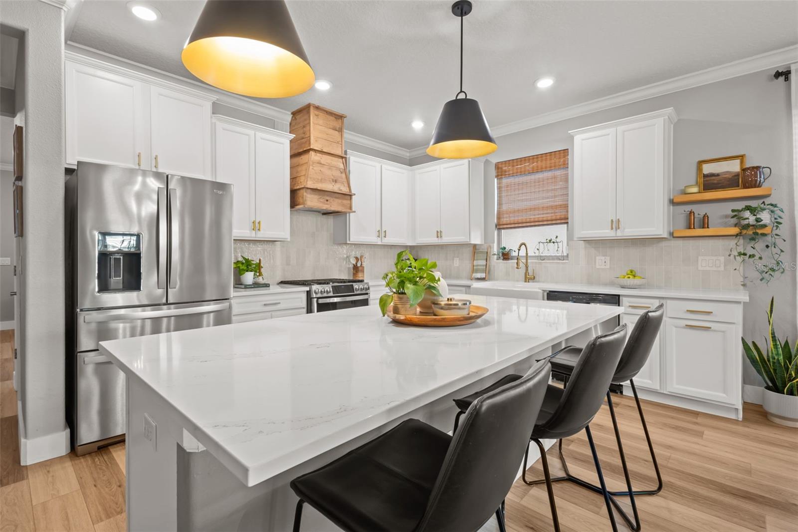 Kitchen has a large quartz island, custom range hood, backspash, stainless steel appliances, and gas range