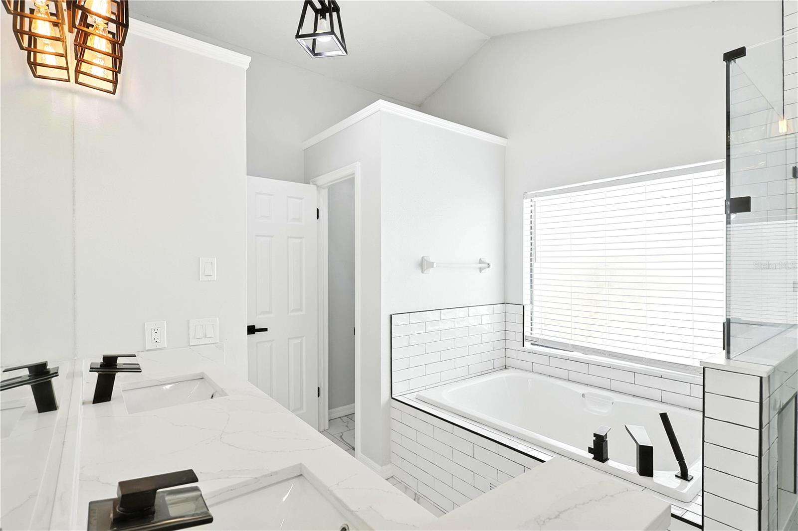 Primary bathroom with double sink, vanities, quartz countertops, standalone tub, and tiled, walk-in shower with glass shower walls