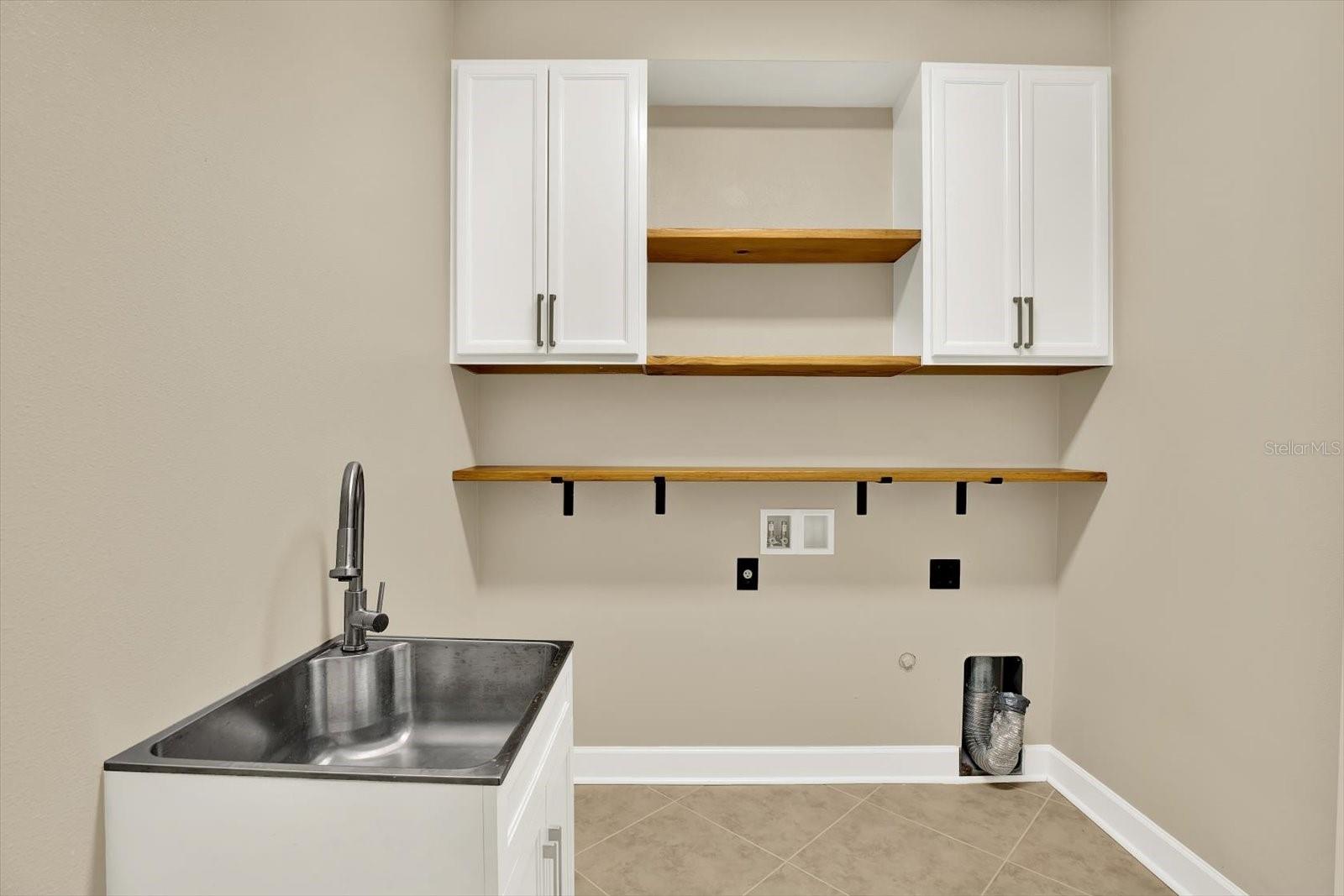 Laundry room features closed cabinets, custom wood shelves and nicely finished utility sink