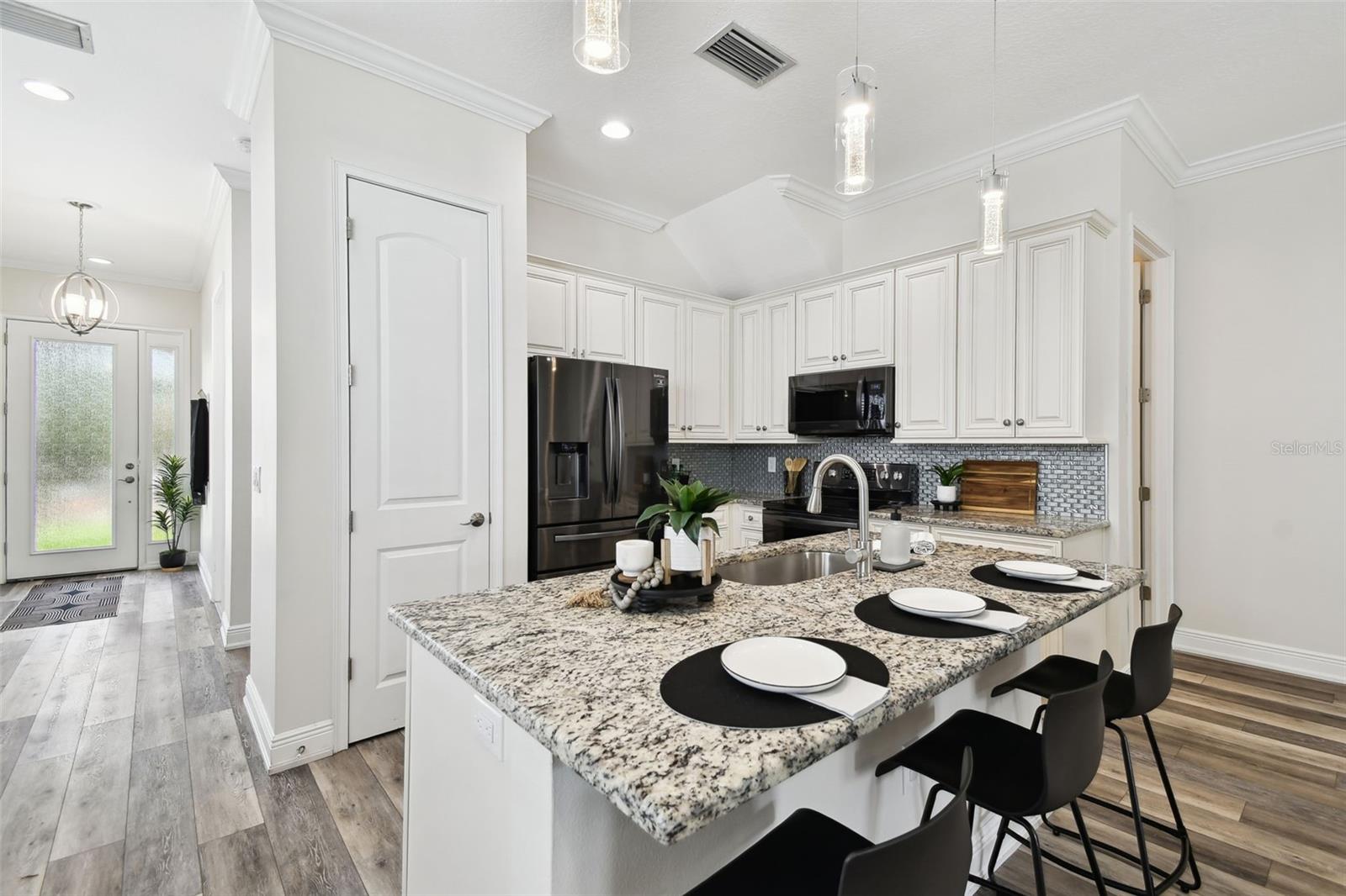 Spacious kitchen with 42" cabinets, granite tops, black stainless appliances, granite, tile backsplash, and custom pendant lighting.