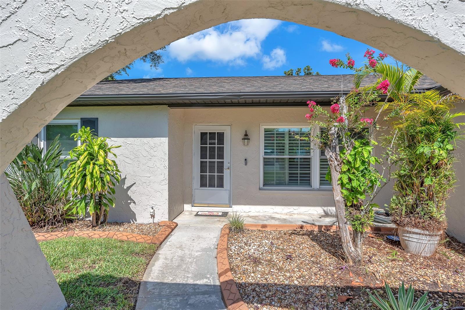 A charming arched walkway guides you to the entrance, surrounded by well-maintained landscaping accented with concrete curbing.