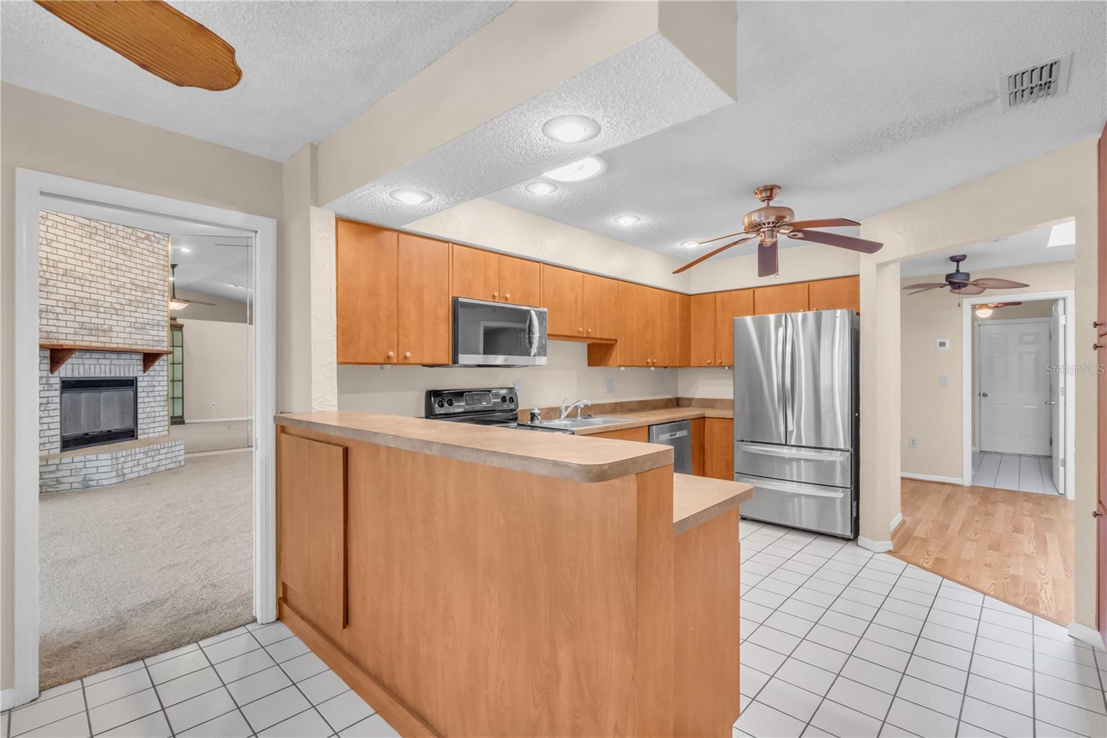 Kitchen with refrigerator and entryway into the Great Room. Ceiling fans in the Kitchen and Kitchen Nook. Solar Tube brightens the Kitchen.