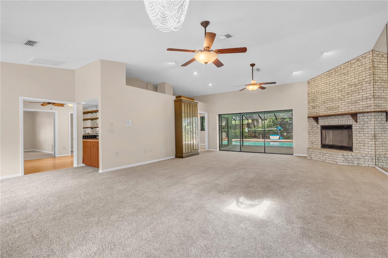 Great Room with fireplace, ceiling fans, and exit to lanai and pool.