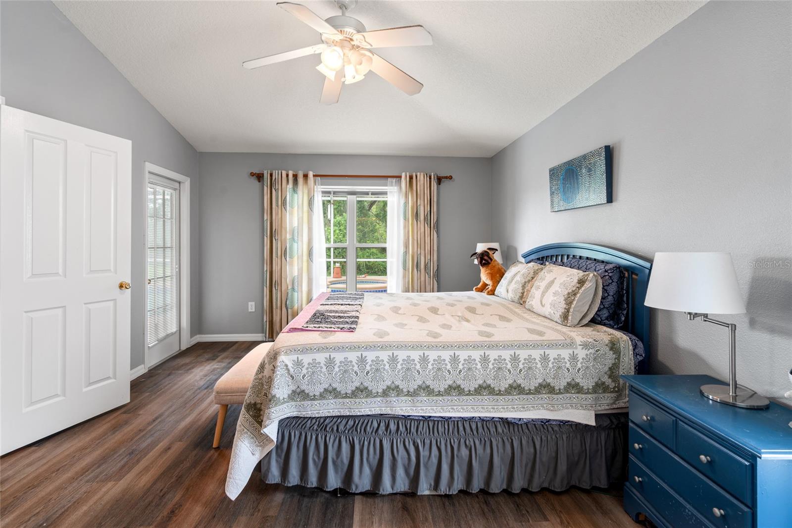 Primary Bedroom w/ newer flooring, a door to the pool area, ceiling fans, 2 closets and an en suite bath