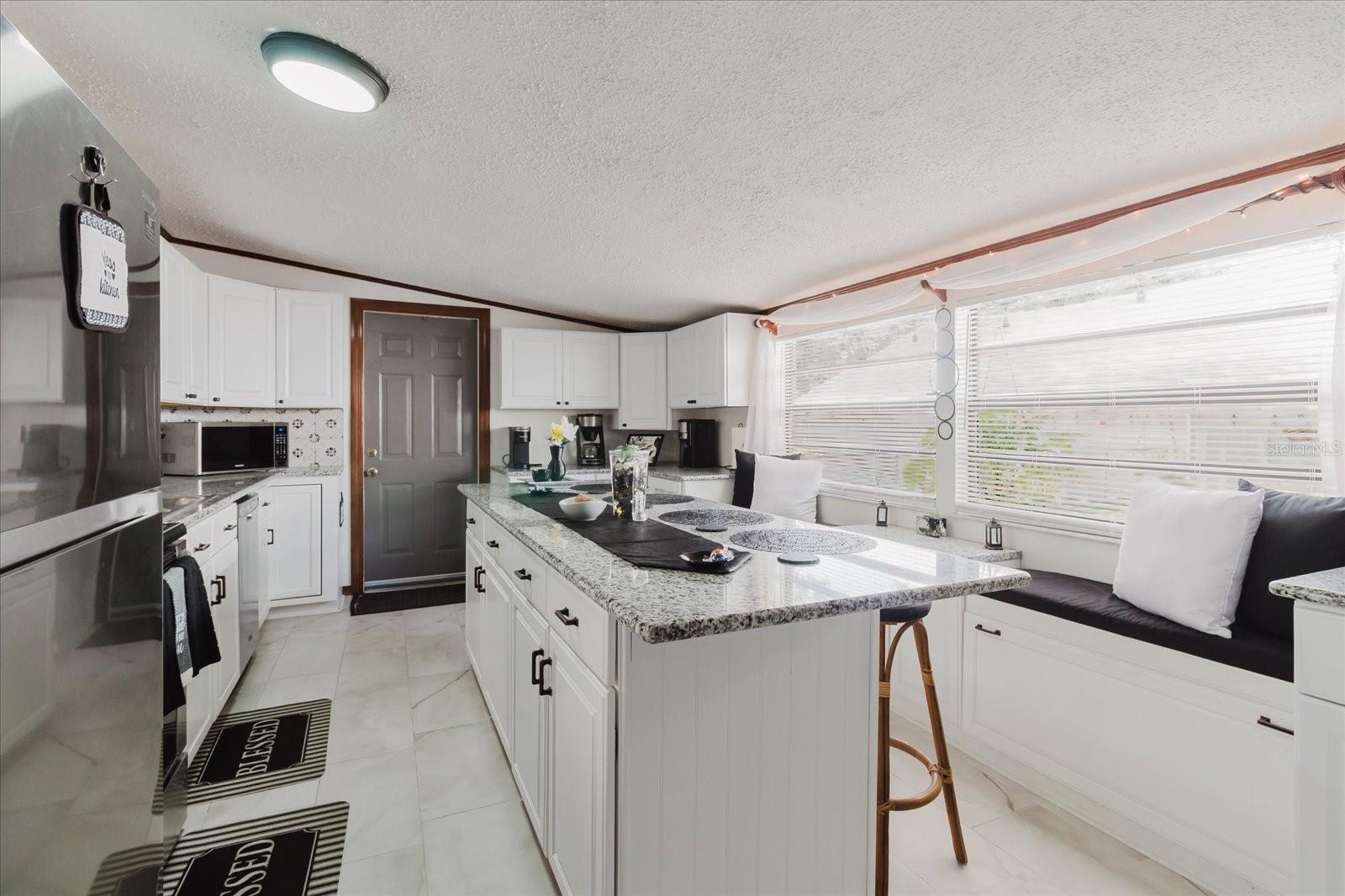 Updated Kitchen With Granite Counters, Stainless Steel Appliances, & Marble Looking Floor Tile. Seating For 4 People At Kitchen Island. Doorway Leads To Backyard and The Laundry Closet. All Kitchen Appliances Stay.