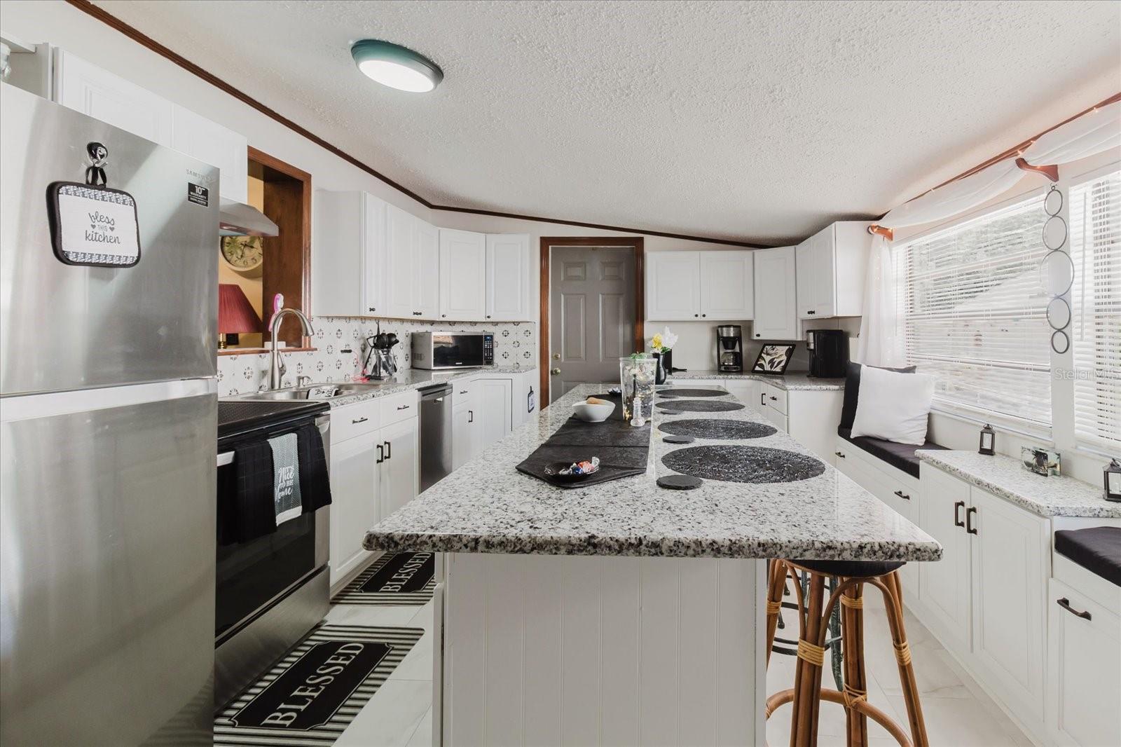 Updated Kitchen With Granite Counters, Stainless Steel Appliances, & Marble Looking Floor Tile. Seating For 4 People At Kitchen Island. Doorway Leads To Backyard and The Laundry Closet. All Kitchen Appliances Stay.