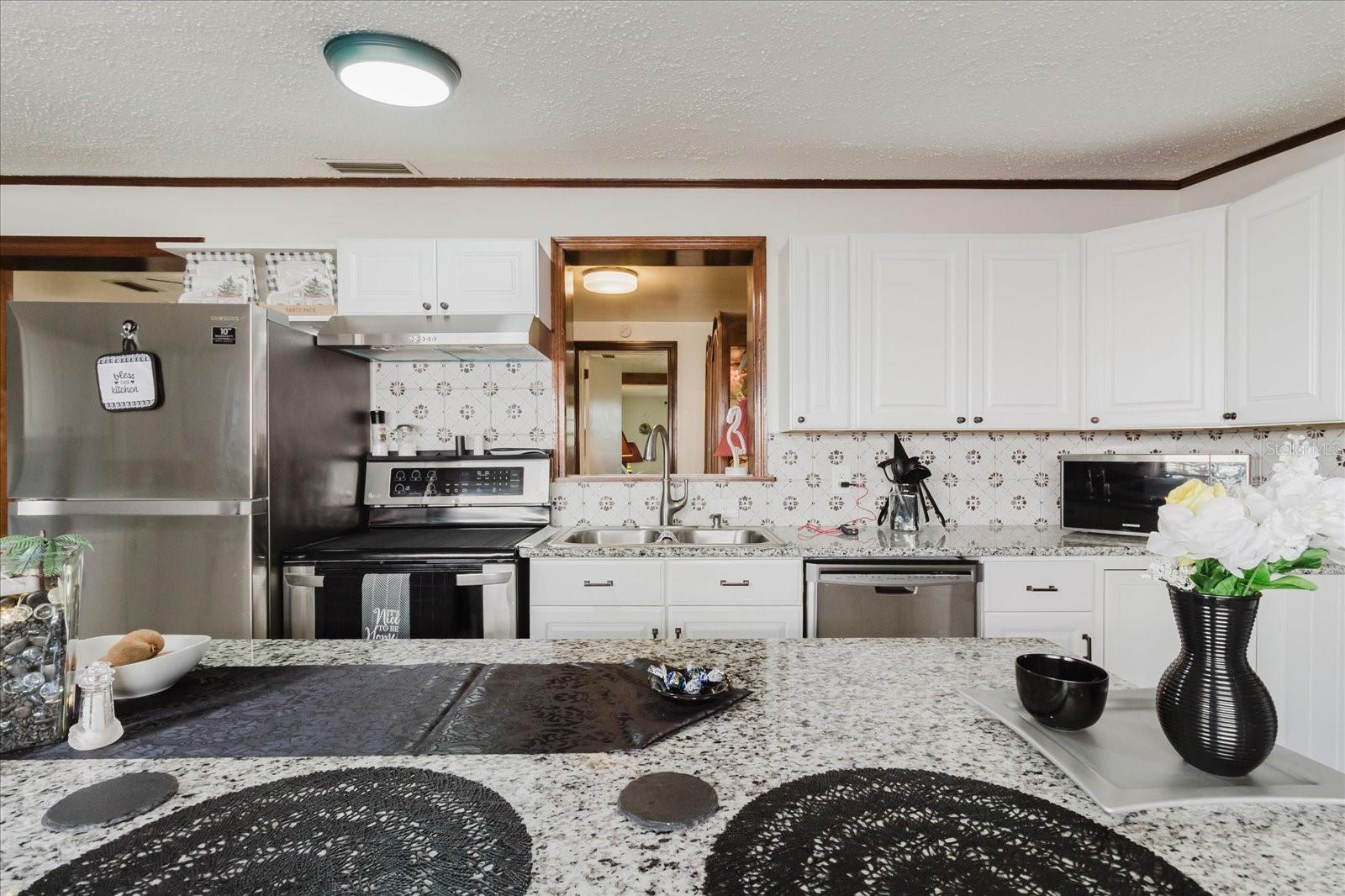 Updated Kitchen With Granite Counters, Stainless Steel Appliances, & Marble Looking Floor Tile. Seating For 4 People At Kitchen Island. Doorway Leads To Backyard and The Laundry Closet. All Kitchen Appliances Stay.