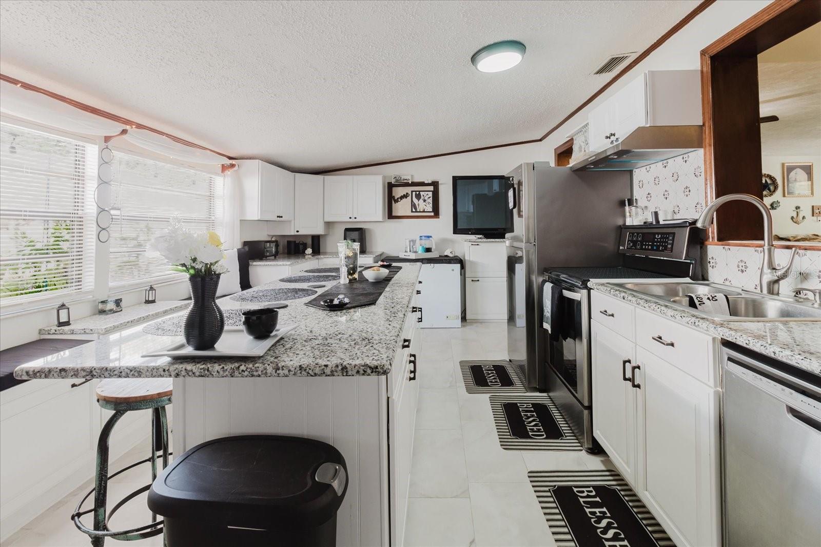 Updated Kitchen With Granite Counters, Stainless Steel Appliances, & Marble Looking Floor Tile. Seating For 4 People At Kitchen Island. Doorway Leads To Backyard and The Laundry Closet. All Kitchen Appliances Stay.